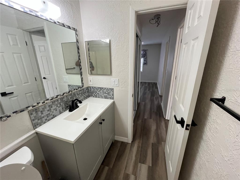 A bathroom features a gray vanity, a mosaic tile backsplash, and wood-look flooring — 6950 ROSEMONT DRIVE UNIT A&B, ENGLEWOOD, FL