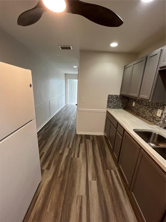 A galley kitchen with gray cabinets and wood-look flooring leads into a hallway — 6950 ROSEMONT DRIVE UNIT A&B, ENGLEWOOD, FL