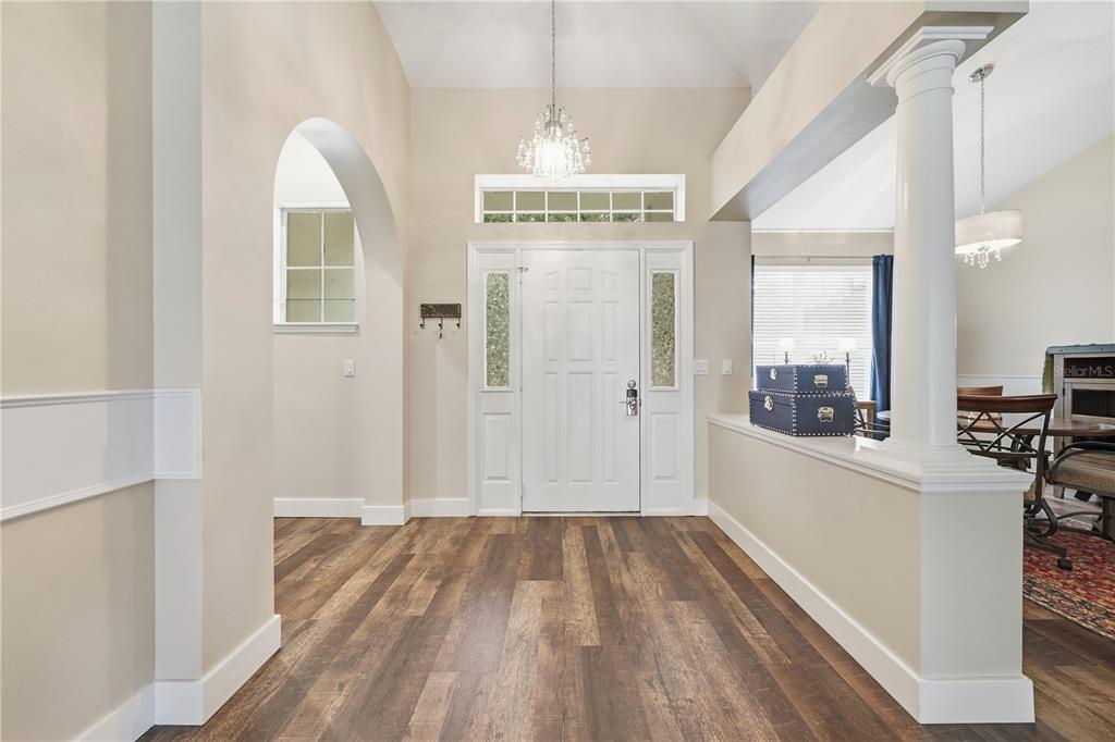 A bright entryway features wood-look flooring, a white front door, and a decorative support column — 2360 PARK FOREST BOULEVARD, MOUNT DORA, FL
