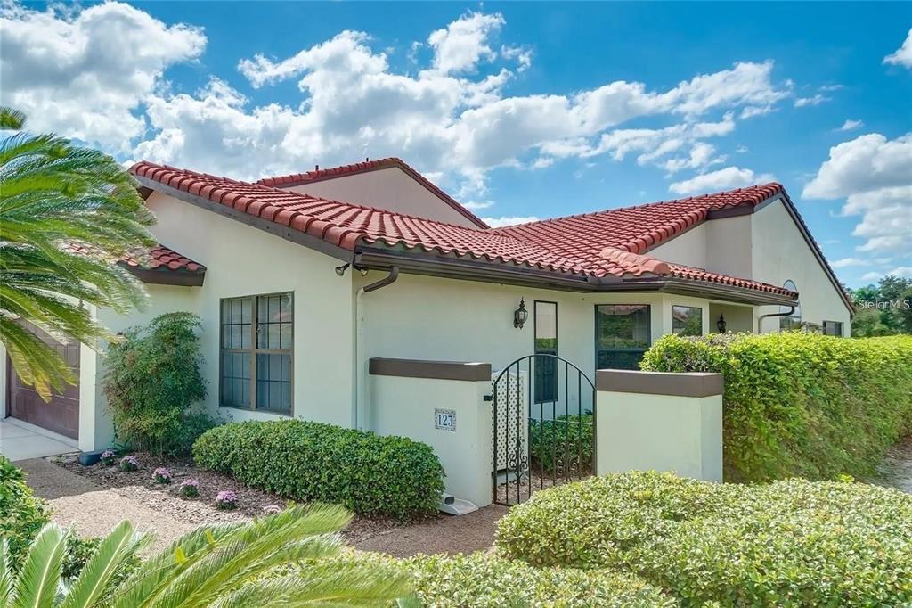 A single-story house with a red tile roof, stucco walls, and a gated courtyard entrance — 123 COVENTRY LANE, HAINES CITY, FL