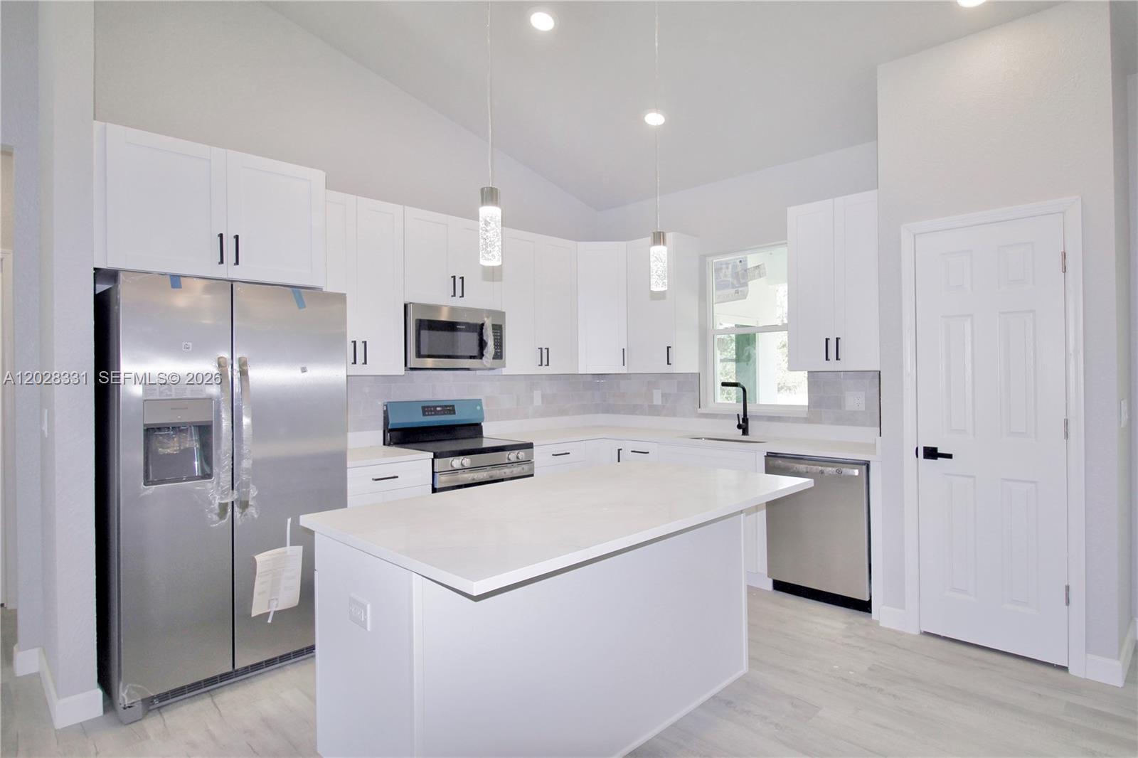 A modern kitchen features white cabinets, stainless steel appliances, a center island, and light flooring — 4000 GARIENDA AVE, Sebring FL 33872, SEBRING, FL