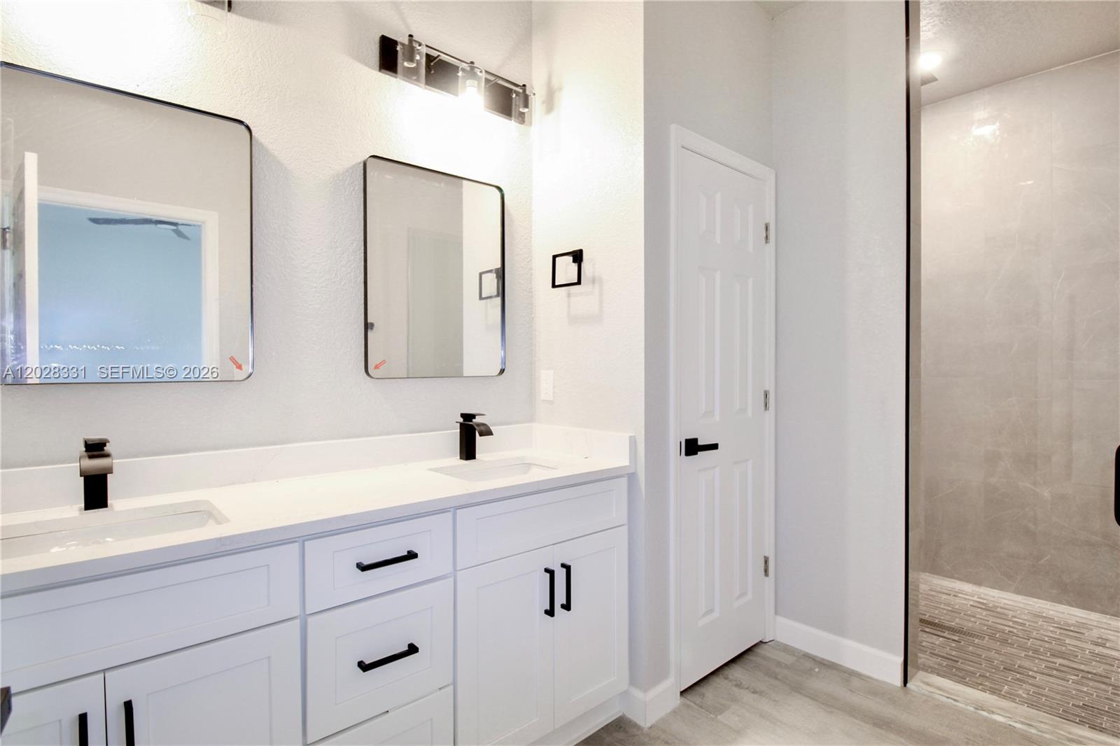 A modern bathroom features a double vanity with white cabinets, black hardware, and a walk-in shower — 4000 GARIENDA AVE, Sebring FL 33872, SEBRING, FL