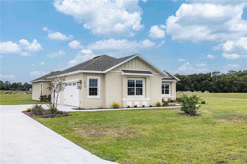 A single-story tan house with a two-car garage sits on a large grassy lot — 1439 CR 212, OXFORD, FL