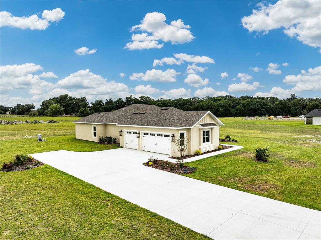 An aerial view of a tan single-story house with a three-car garage and concrete driveway — 1439 CR 212, OXFORD, FL