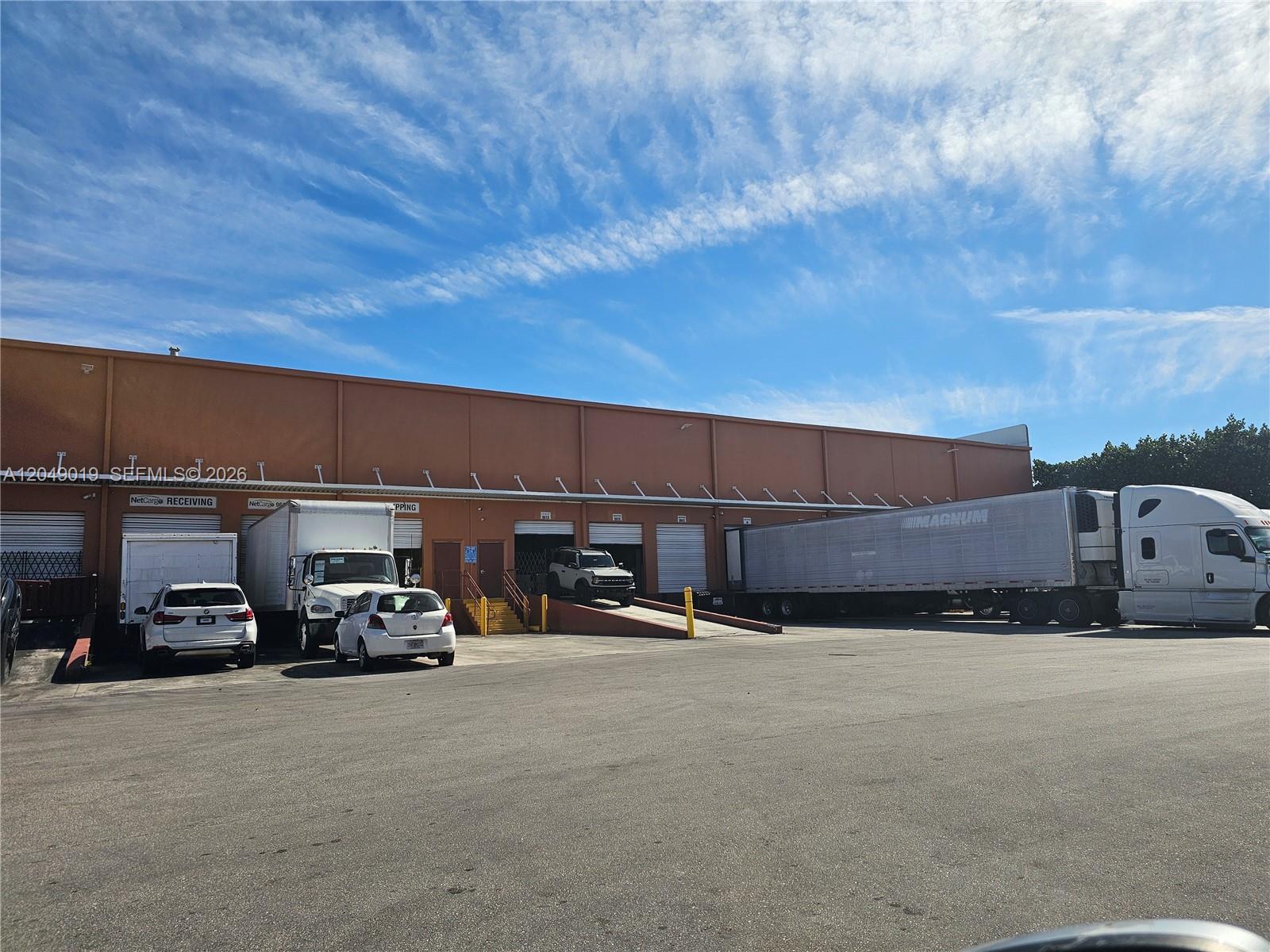 An exterior view of a commercial warehouse building with loading docks and parked vehicles — 9613 NW 33rd St, Doral FL 33172, DORAL, FL
