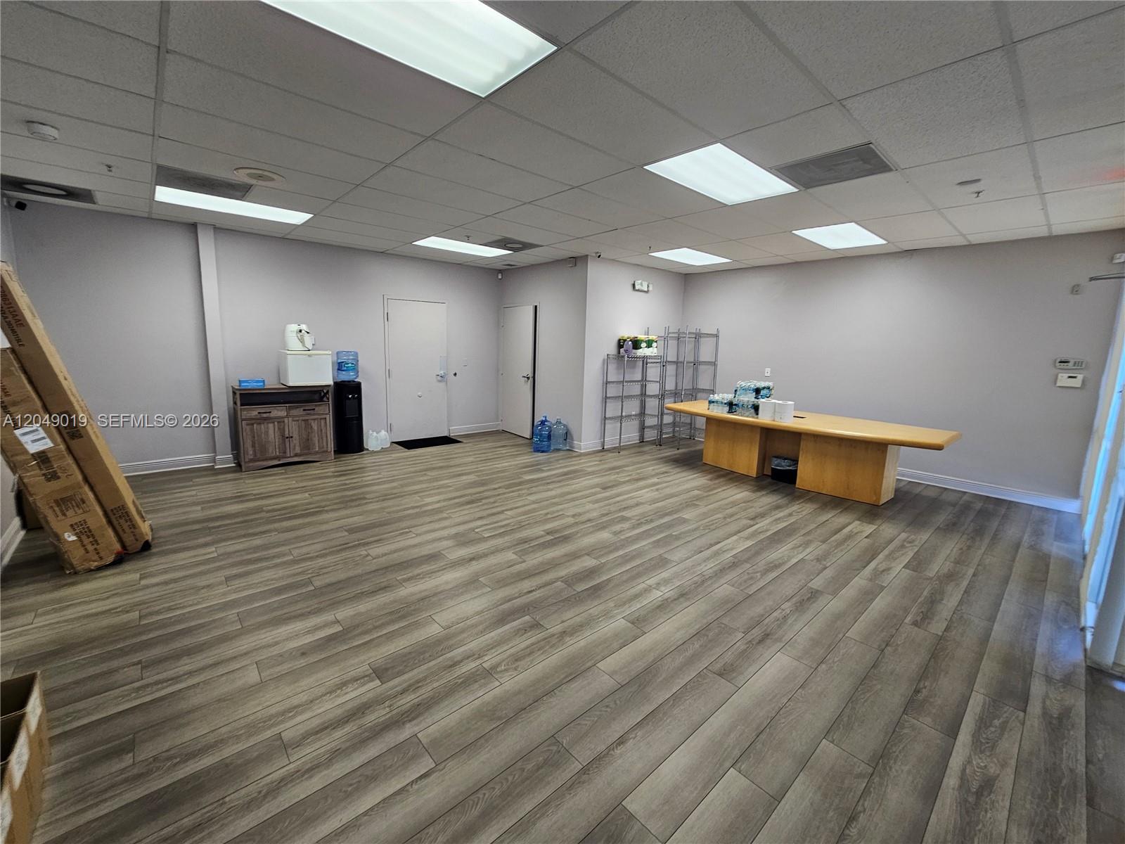 An office space features light gray walls, wood-look flooring, a central table, and storage shelving — 9613 NW 33rd St, Doral FL 33172, DORAL, FL