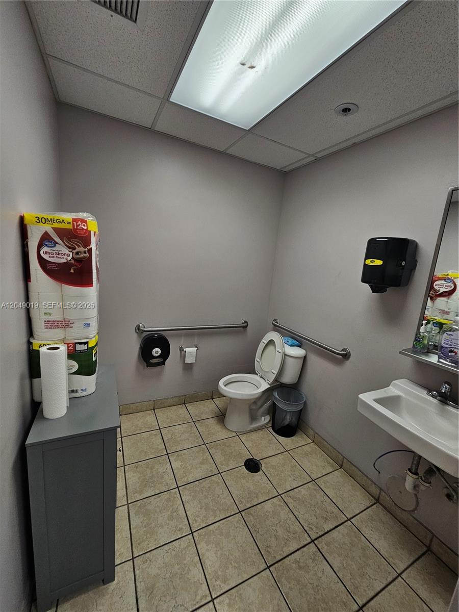 A small, tiled commercial restroom features a toilet, a sink, and stacks of paper products — 9613 NW 33rd St, Doral FL 33172, DORAL, FL