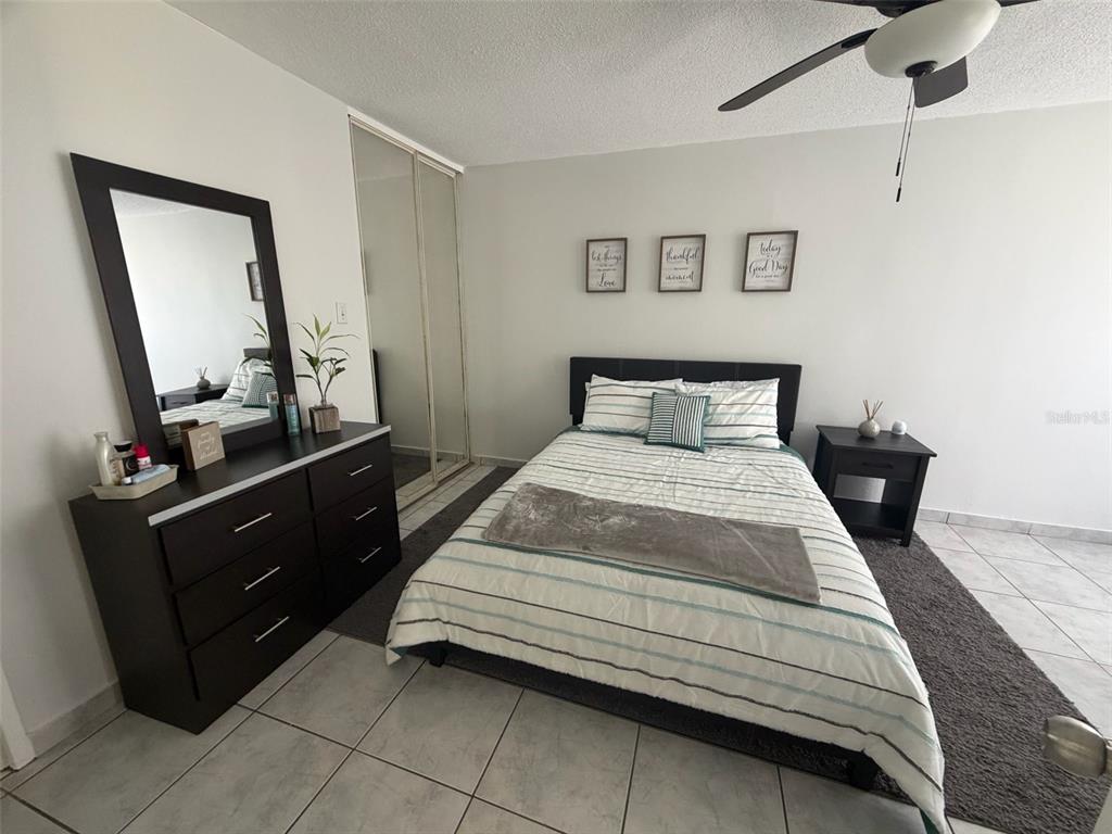 A bedroom features a bed with striped bedding, a dark dresser with a mirror, and tile flooring — Islote Cayo Obispo ISLETA MARINA UNIT 6-S, FAJARDO, PR