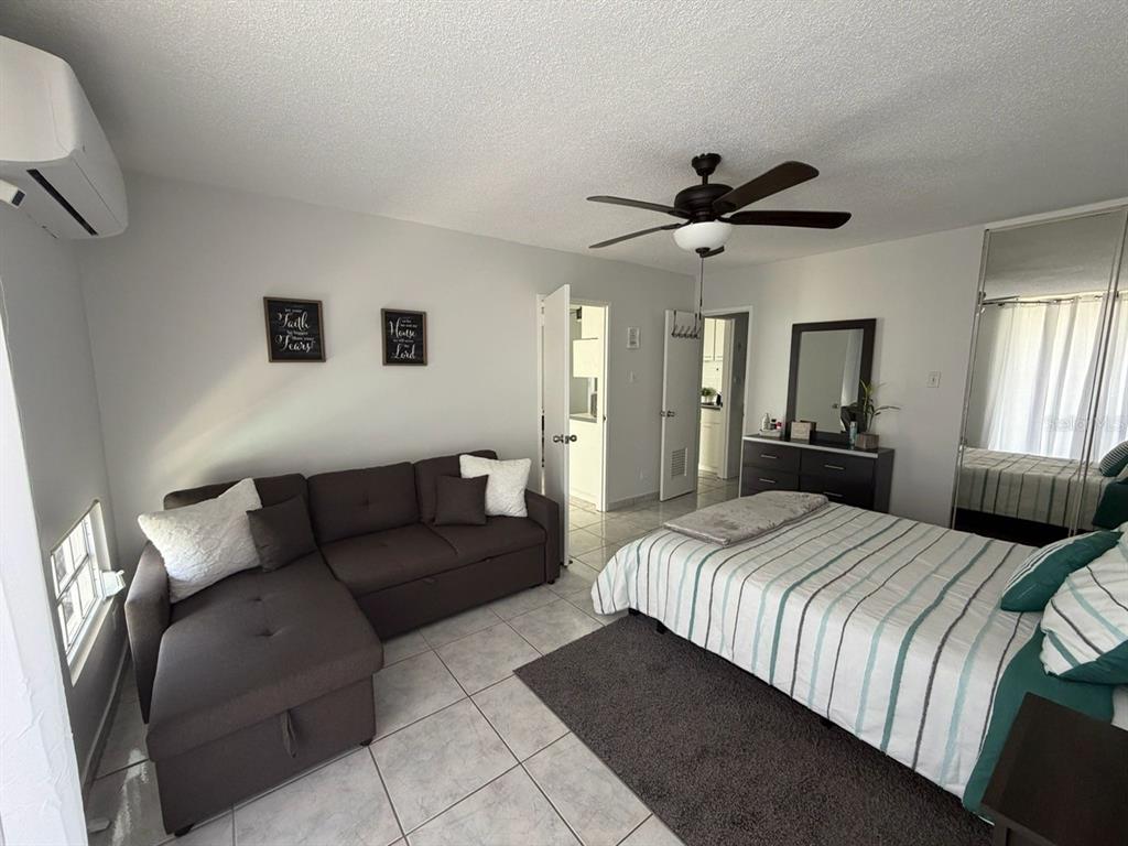 A bedroom features a sectional sofa, a bed with striped bedding, and tile flooring — Islote Cayo Obispo ISLETA MARINA UNIT 6-S, FAJARDO, PR