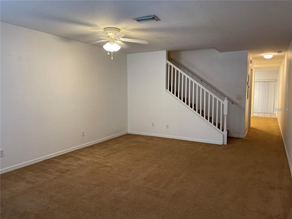 A carpeted living room features a white staircase, a ceiling fan, and plain white walls — 10806 BRICKSIDE COURT, RIVERVIEW, FL
