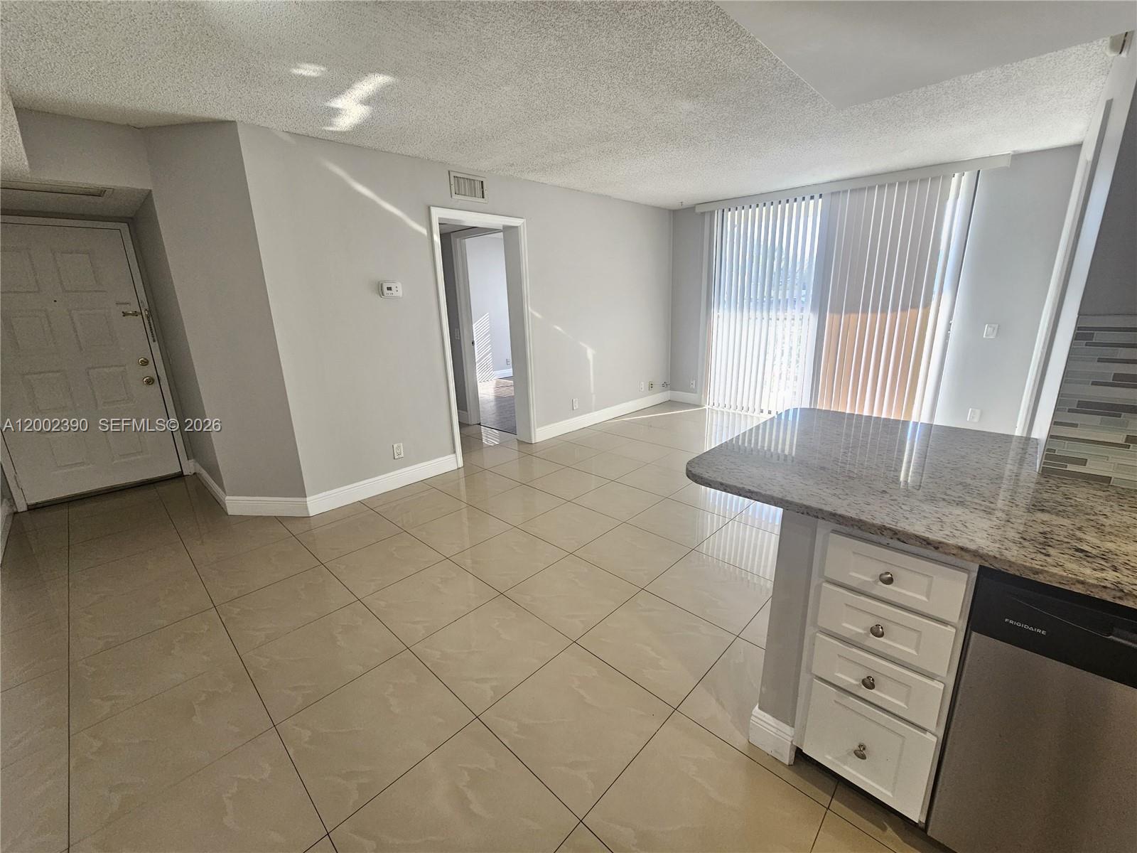 A kitchen island with granite countertops overlooks a living area with tile floors and blinds — 734 Executive Center Dr # 12, West Palm Beach FL 33401, WEST PALM BEACH, FL
