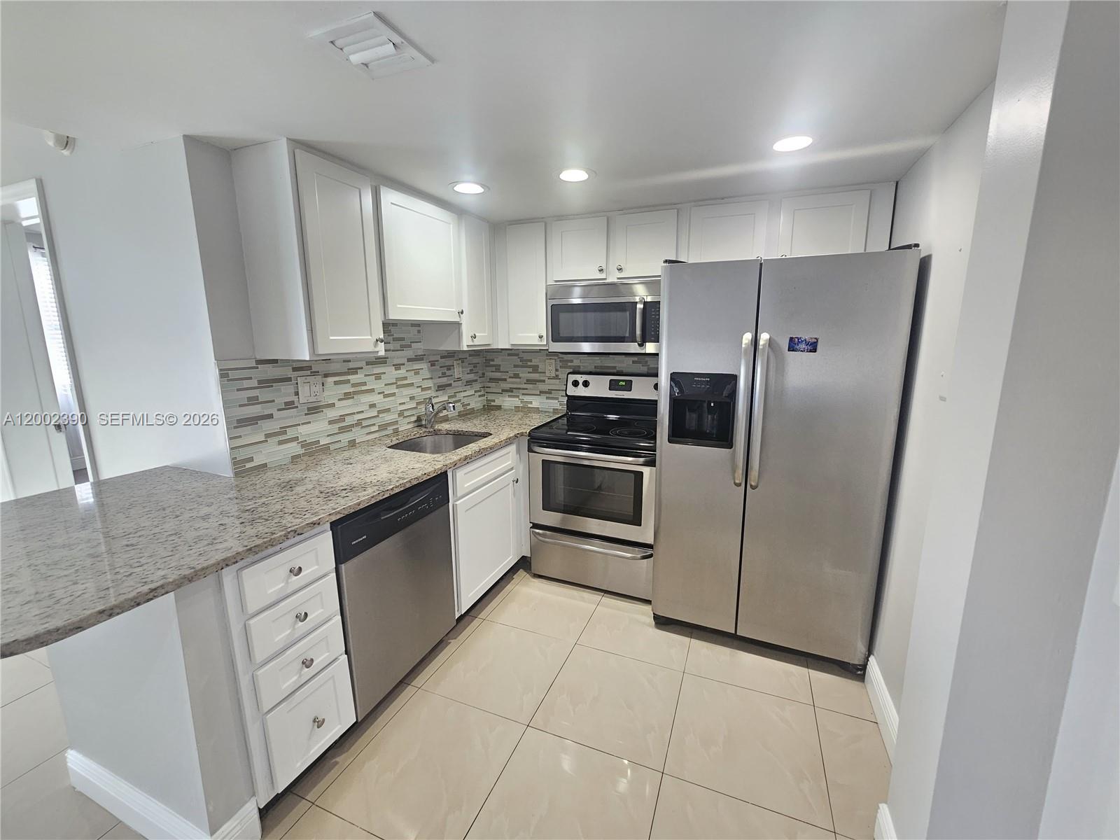 A kitchen features white cabinets, granite countertops, stainless steel appliances, and light tile flooring — 734 Executive Center Dr # 12, West Palm Beach FL 33401, WEST PALM BEACH, FL