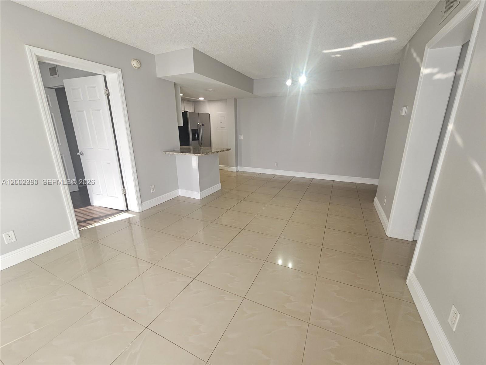 An open-concept living area features light gray walls, large beige floor tiles, and a kitchen — 734 Executive Center Dr # 12, West Palm Beach FL 33401, WEST PALM BEACH, FL