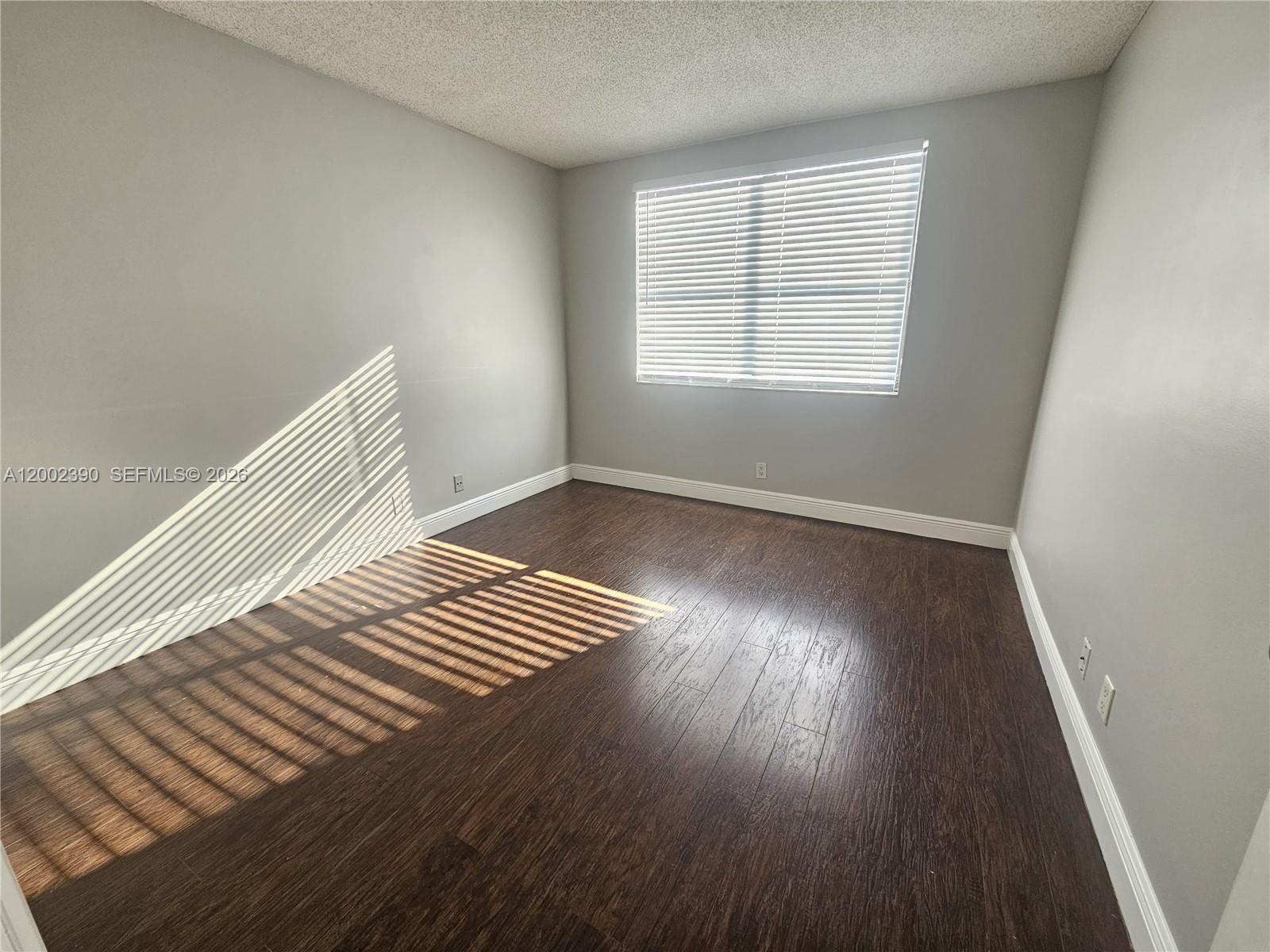 An empty room features gray walls, dark wood-look flooring, and a window with white blinds — 734 Executive Center Dr # 12, West Palm Beach FL 33401, WEST PALM BEACH, FL