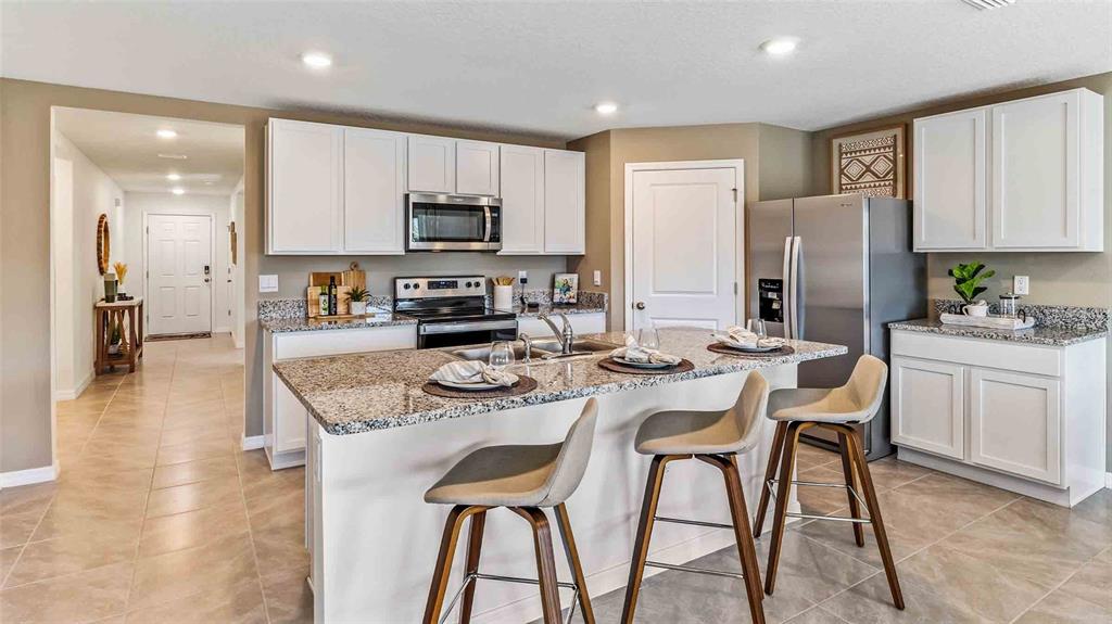A kitchen features white cabinets, granite countertops, a central island with bar stools, and appliances — 35100 VALLEY RIDGE ROAD, DADE CITY, FL