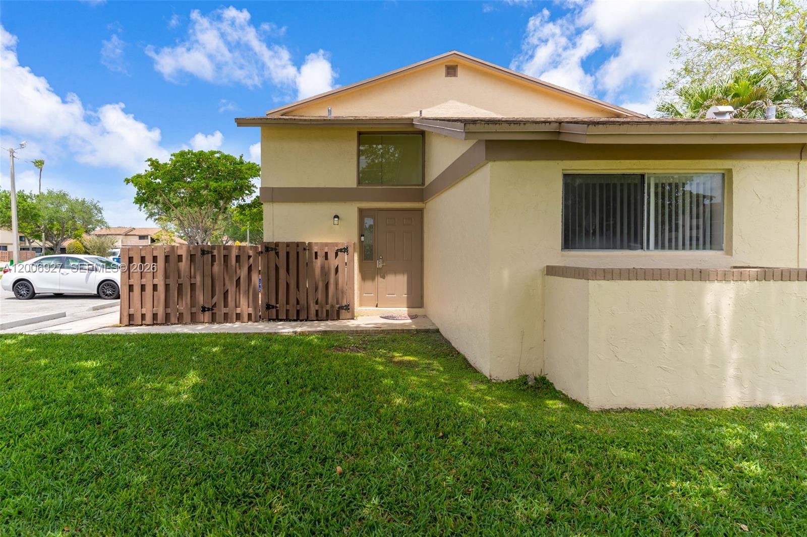 A two-story tan stucco townhouse features a brown wooden fence and a small front lawn — 2950 NW 106th ave # 10, Sunrise FL 33322, SUNRISE, FL