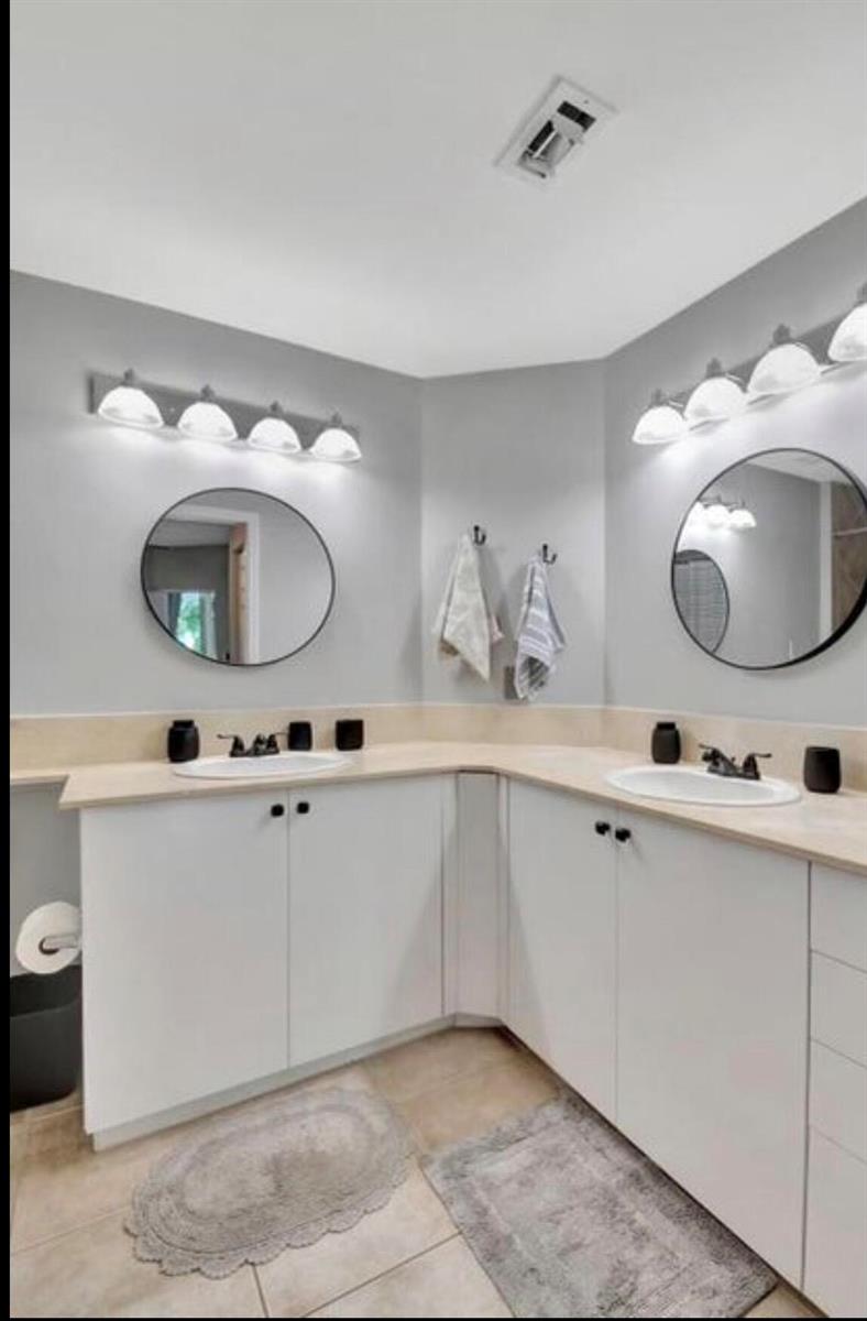 A bathroom features a corner vanity with dual sinks, white cabinets, and two round mirrors — 804 E Windward Way # 316, Lantana FL 33462, LANTANA, FL