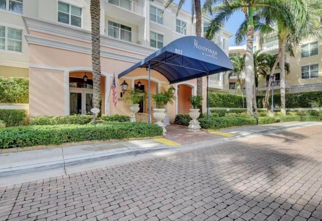 The exterior entrance of a multi-story residential building features a blue awning and palm trees — 804 E Windward Way # 316, Lantana FL 33462, LANTANA, FL