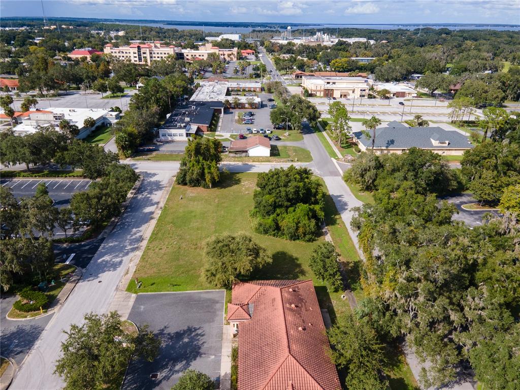An aerial view shows a vacant lot surrounded by commercial buildings, parking lots, and trees — 700 PHYSICIANS COURT, LEESBURG, FL