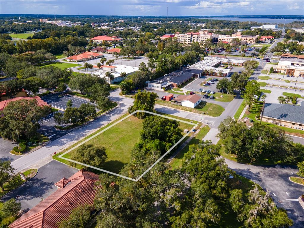 An aerial view shows a vacant rectangular lot outlined in white surrounded by commercial buildings — 700 PHYSICIANS COURT, LEESBURG, FL