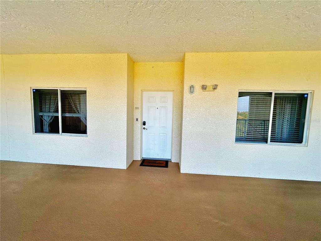 A white front door is centered between two windows on a covered exterior walkway — 6336 BUFORD STREET UNIT 605, ORLANDO, FL