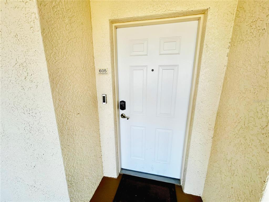 A white front door with a digital lock is set into a textured beige wall — 6336 BUFORD STREET UNIT 605, ORLANDO, FL
