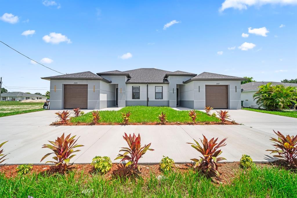 A front view of a modern duplex with two garages, concrete driveways, and landscaped beds — 1315/1317 DIPLOMAT PARKWAY E, CAPE CORAL, FL
