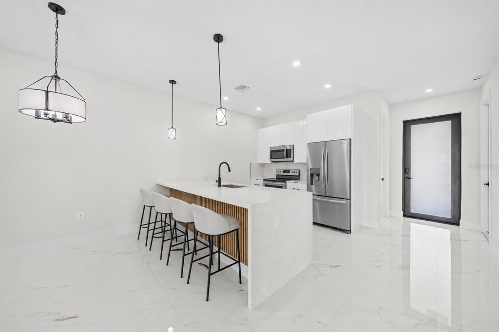 A modern kitchen features a white quartz island with wood slats, barstools, and marble flooring — 1315/1317 DIPLOMAT PARKWAY E, CAPE CORAL, FL
