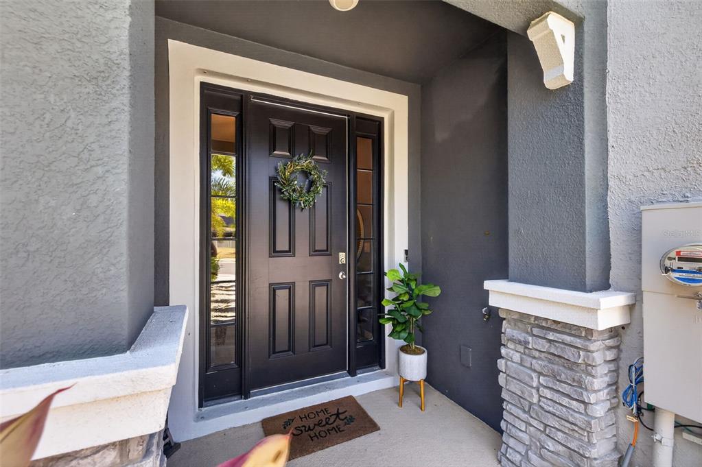 A dark front door with sidelights and a wreath sits under a covered entryway — 6544 CALYPSO CORAL LANE, SARASOTA, FL