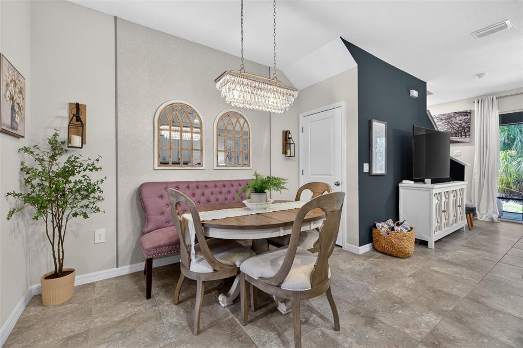 A dining area features a tufted purple bench, round wooden table, and a crystal chandelier — 6544 CALYPSO CORAL LANE, SARASOTA, FL