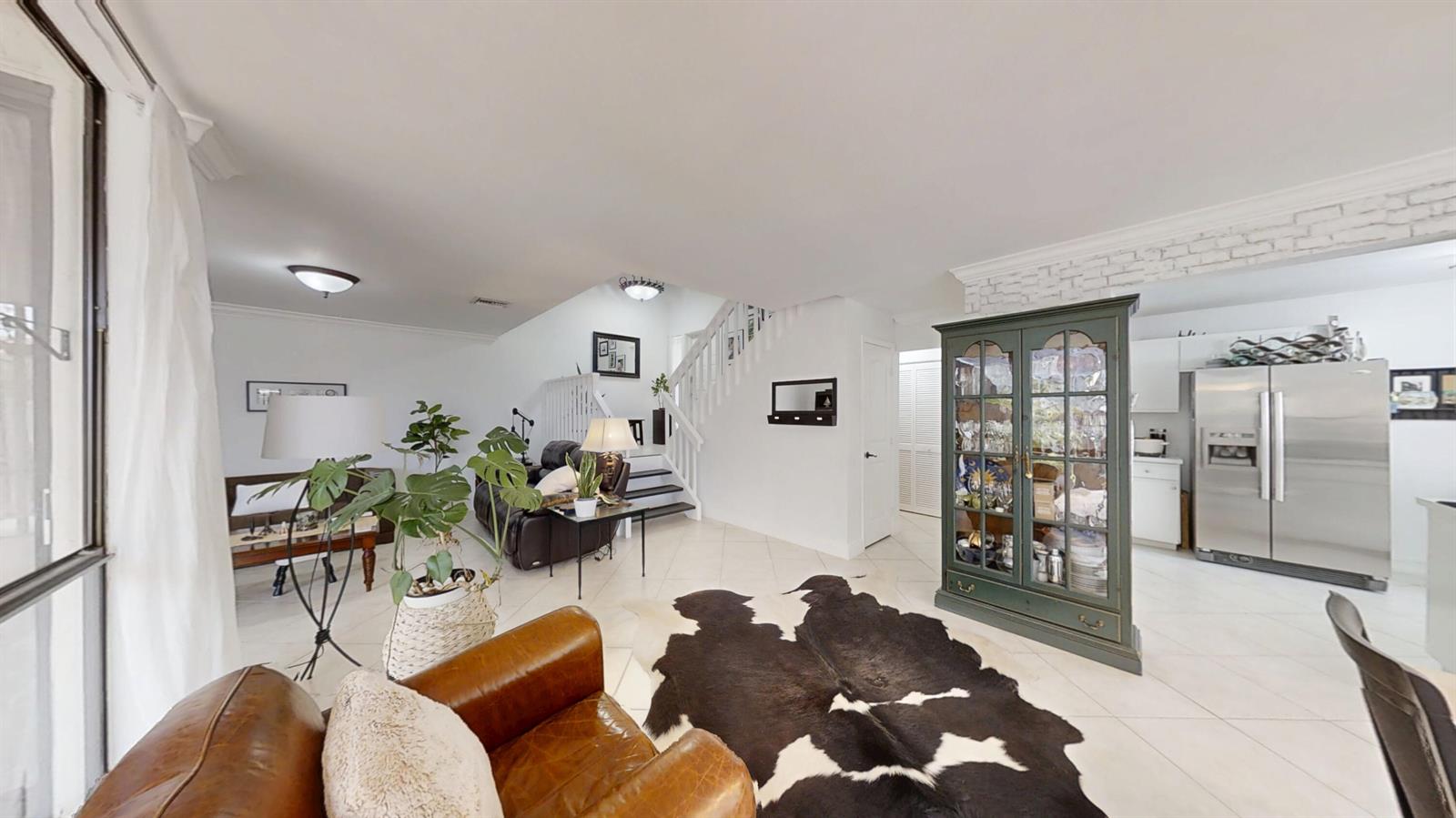 A living room with tile floors, a cowhide rug, a staircase, and a glass-front cabinet — 5803 Fox Hollow Drive # B, Boca Raton FL 33486, BOCA RATON, FL