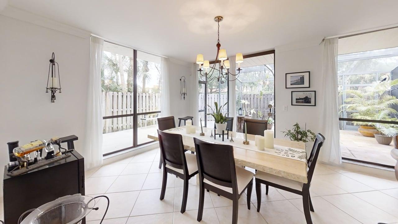 A dining room features a stone-topped table, dark chairs, a chandelier, and large glass doors — 5803 Fox Hollow Drive # B, Boca Raton FL 33486, BOCA RATON, FL