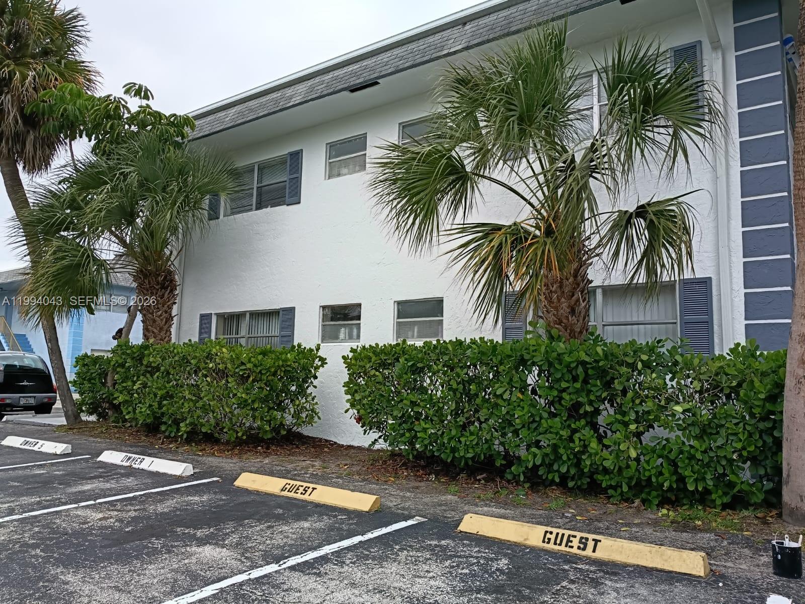 A two-story white apartment building features palm trees and designated guest parking spaces in front — 1001 NW 45th St # 6, Deerfield Beach FL 33064, DEERFIELD BEACH, FL