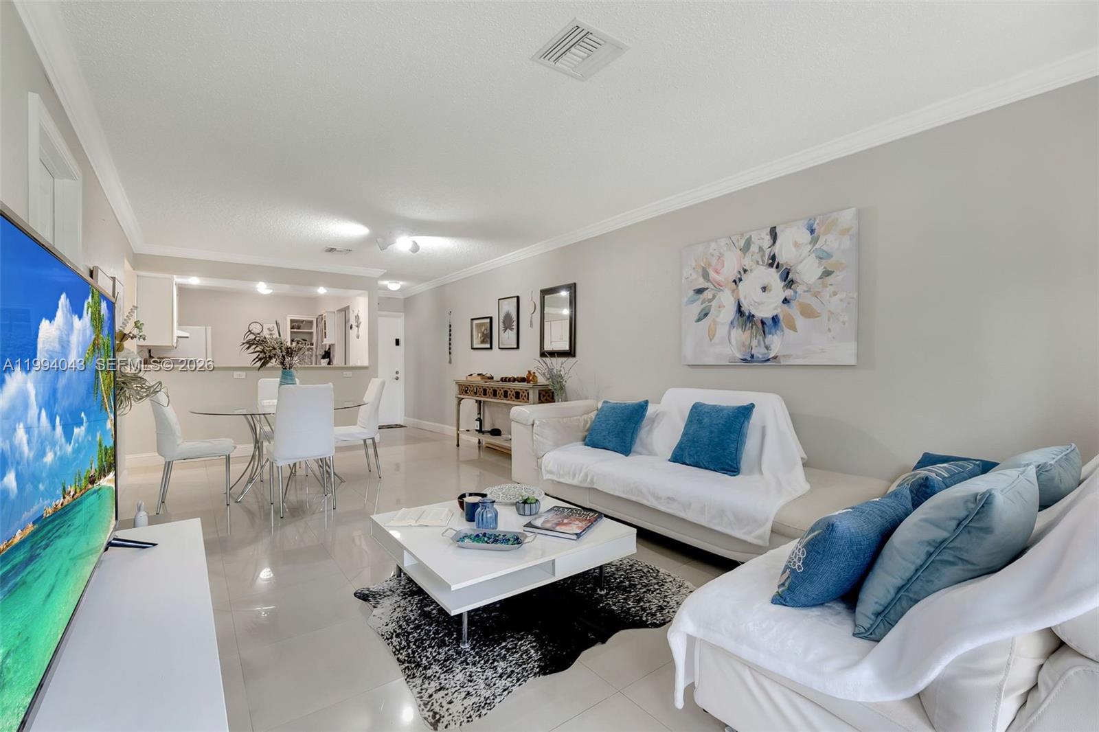 A living room features white sofas with blue pillows, a coffee table, and tile flooring — 1001 NW 45th St # 6, Deerfield Beach FL 33064, DEERFIELD BEACH, FL