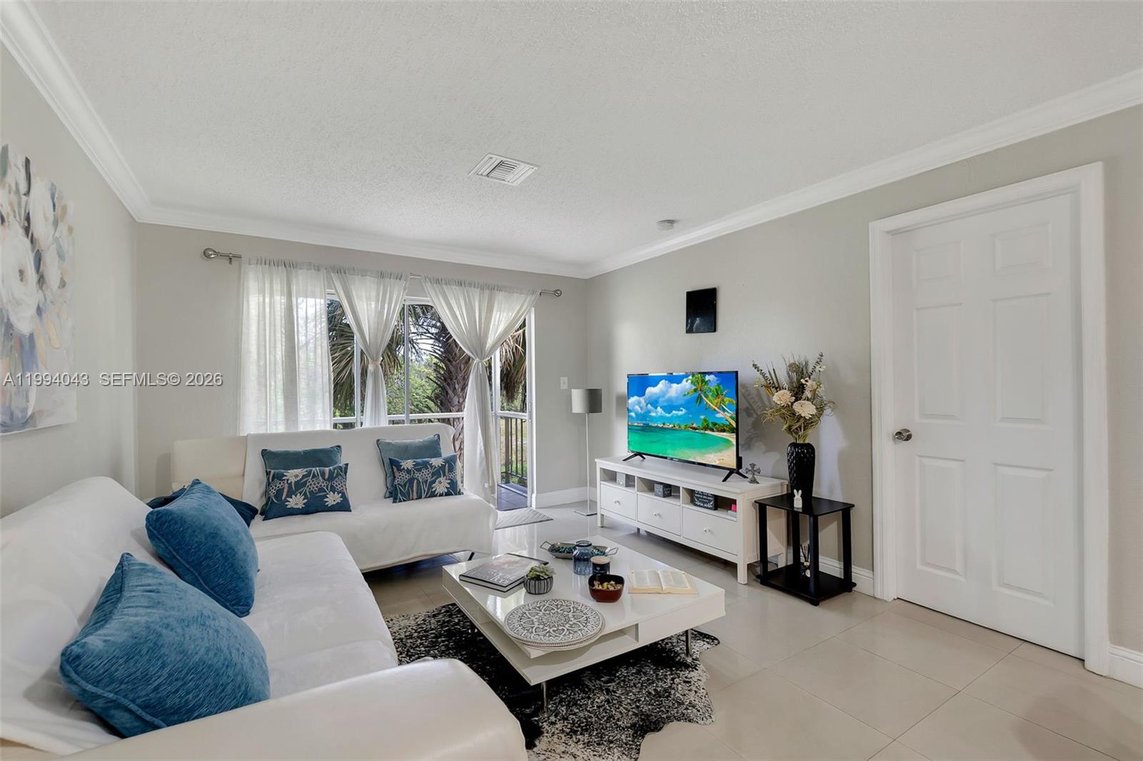 A living room features a white sofa, a coffee table, and a television on a stand — 1001 NW 45th St # 6, Deerfield Beach FL 33064, DEERFIELD BEACH, FL