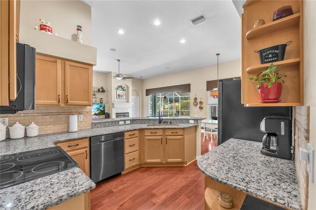 A kitchen with light wood cabinets, granite countertops, and stainless steel appliances overlooks a living area — 2219 LONGMORE CIRCLE, VALRICO, FL