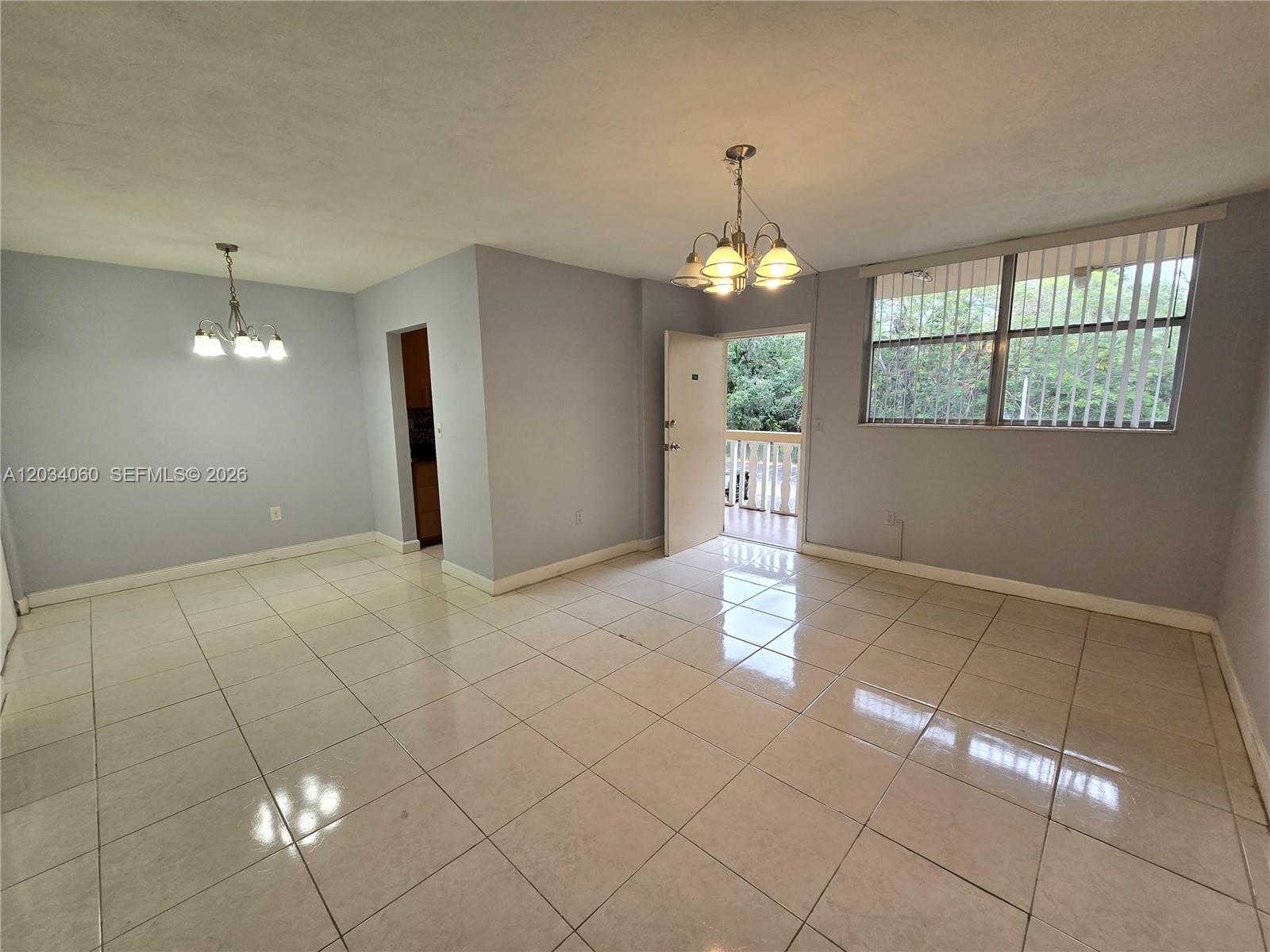 An open living area features light-colored tile flooring, two chandeliers, and a door leading outside — 1475 NE 125th Ter # B, North Miami FL 33161, NORTH MIAMI, FL