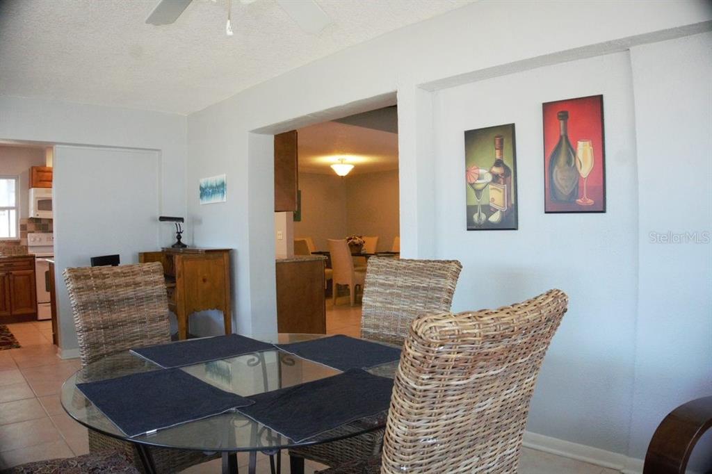 A dining area with a glass-topped table, wicker chairs, and wall art leads to a kitchen — 3139 CARLOS DRIVE, DUNEDIN, FL