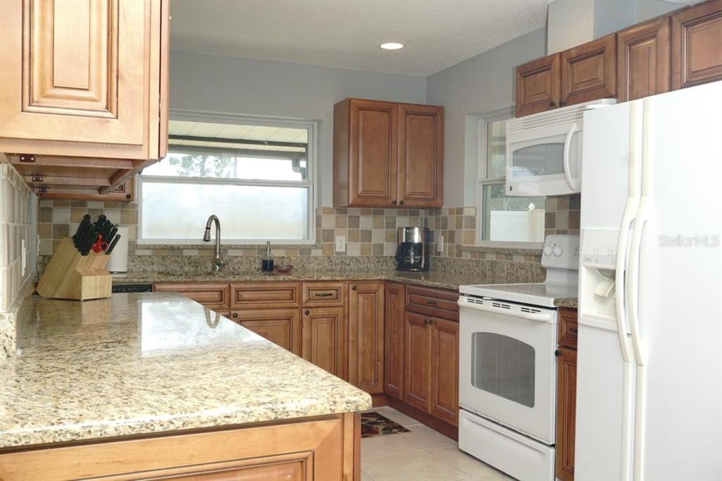 A kitchen features wood cabinets, granite countertops, a tiled backsplash, and white appliances — 3139 CARLOS DRIVE, DUNEDIN, FL