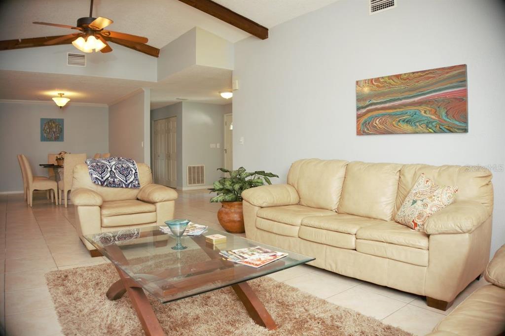 A living room with a beige sofa, armchair, glass coffee table, and vaulted ceiling — 3139 CARLOS DRIVE, DUNEDIN, FL