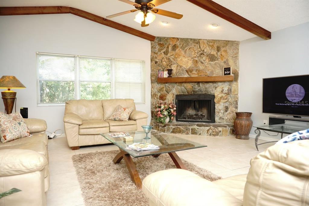 A living room features a stone fireplace, vaulted ceiling with wood beams, and tile flooring — 3139 CARLOS DRIVE, DUNEDIN, FL