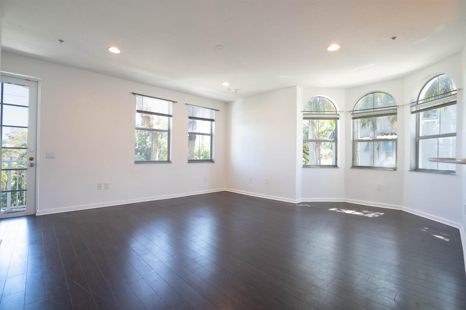 An empty living room with dark wood floors, white walls, and several large windows — 1356 Piazza Pitti, Boynton Beach FL 33426, BOYNTON BEACH, FL