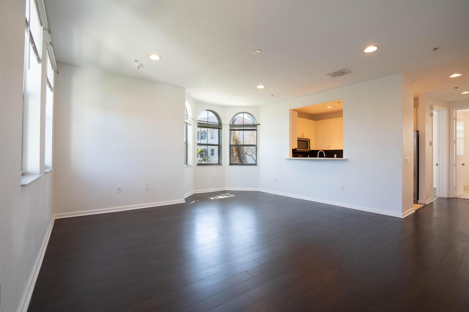An empty living room features dark hardwood floors, white walls, and arched windows — 1356 Piazza Pitti, Boynton Beach FL 33426, BOYNTON BEACH, FL
