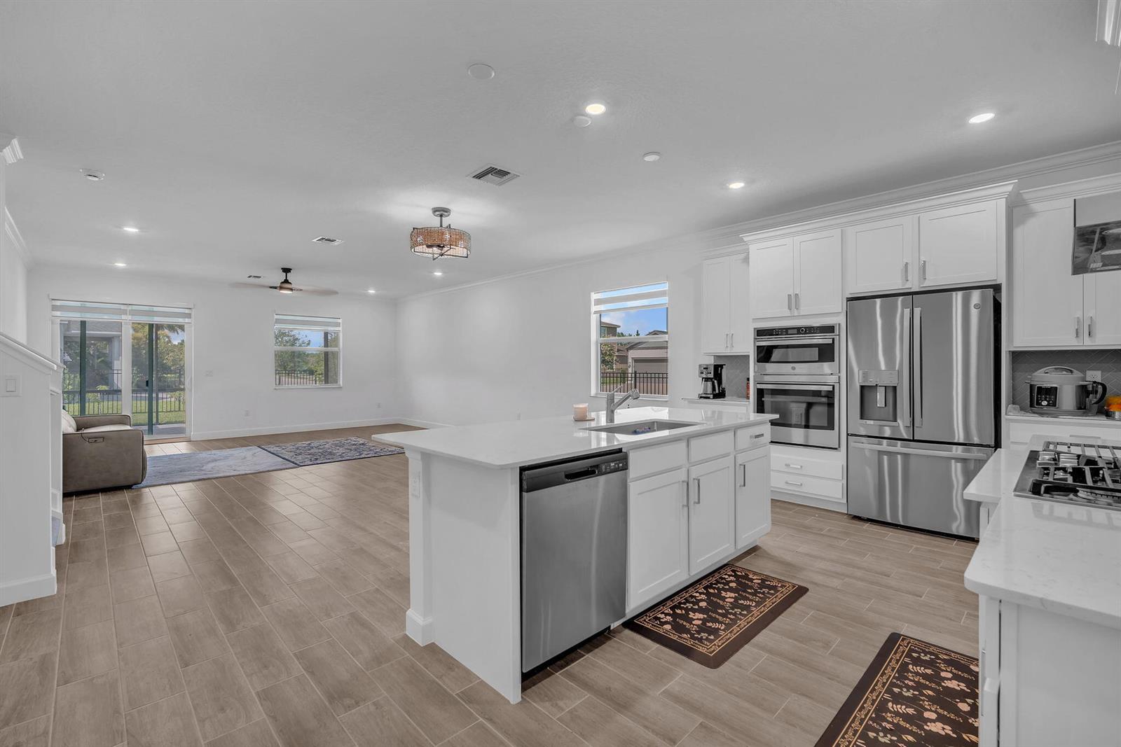 A modern open-concept kitchen features white cabinetry, stainless steel appliances, and a central island — 19270 Rolling Acres Road, FL 33470, FL