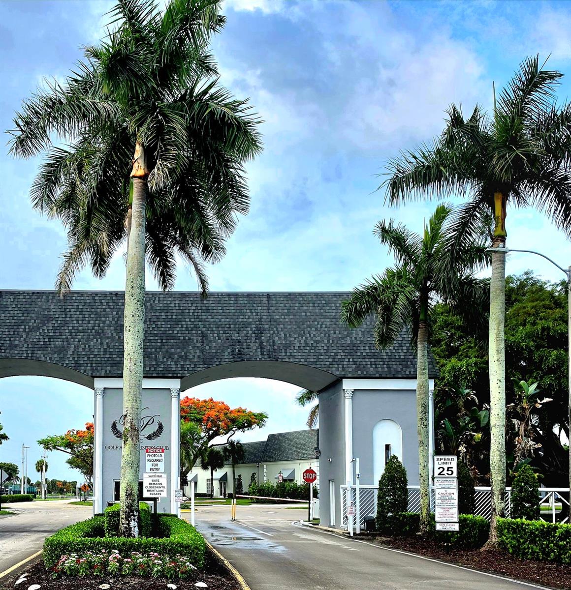 A gated entrance with two palm trees, a gray stone archway, and a speed limit sign — 719 Flanders O, Delray Beach FL 33484, DELRAY BEACH, FL