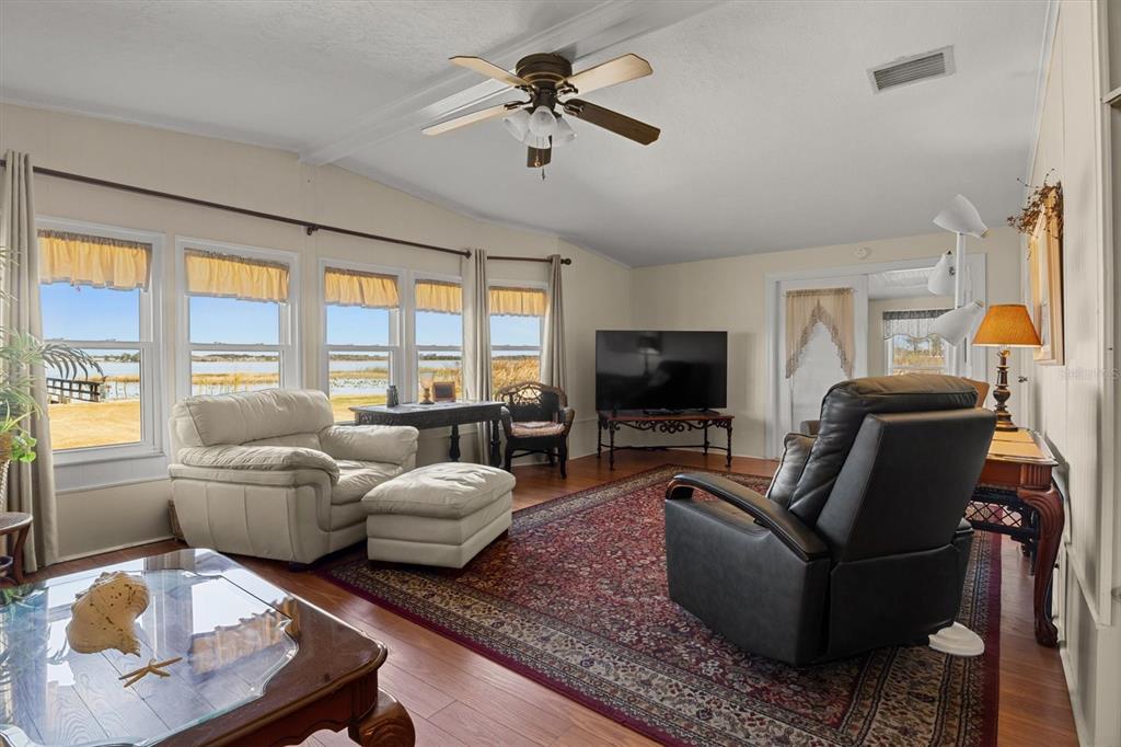 A living room features a ceiling fan, wood flooring, a large rug, and lake views — 6825 S LAKE HENRY DRIVE NE, WINTER HAVEN, FL