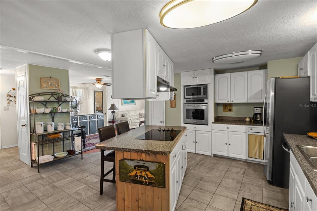 A kitchen features white cabinetry, a central island with a cooktop, and tile flooring — 6825 S LAKE HENRY DRIVE NE, WINTER HAVEN, FL