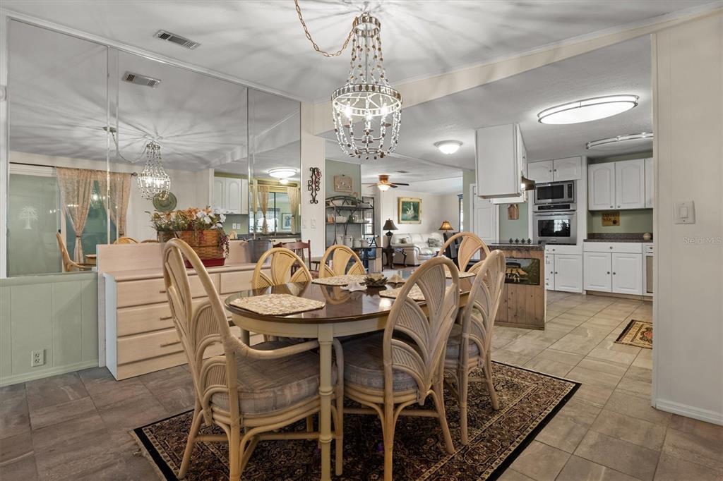 A dining area with a wicker chair set and chandelier opens into a white kitchen — 6825 S LAKE HENRY DRIVE NE, WINTER HAVEN, FL