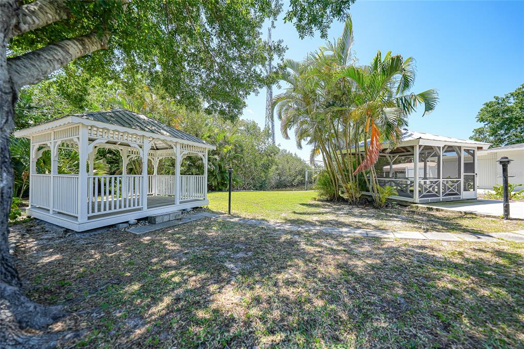 Two white gazebos sit on a grassy lawn near palm trees and mature foliage — 425 FIREBALL COURT, PUNTA GORDA, FL