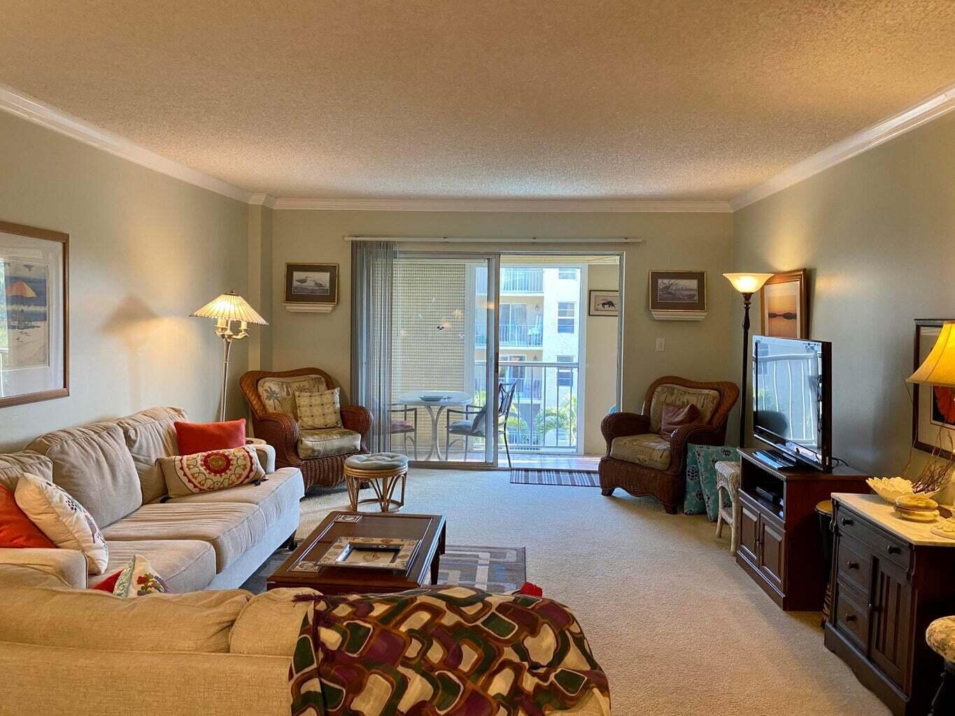 A living room features a beige sofa, two wicker chairs, a television, and a balcony door — 950 Ponce De Leon Road # 309, Boca Raton FL 33432, BOCA RATON, FL